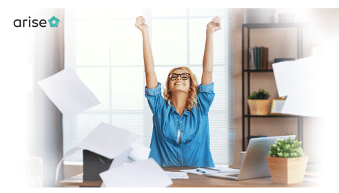 Woman sitting at desk, smiling, with her hands in the air.