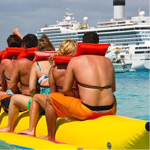 Five people on a floating banana next to a cruise ship.