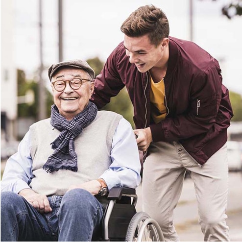 Smiling man pushing a smiling, older man in a wheelchair.