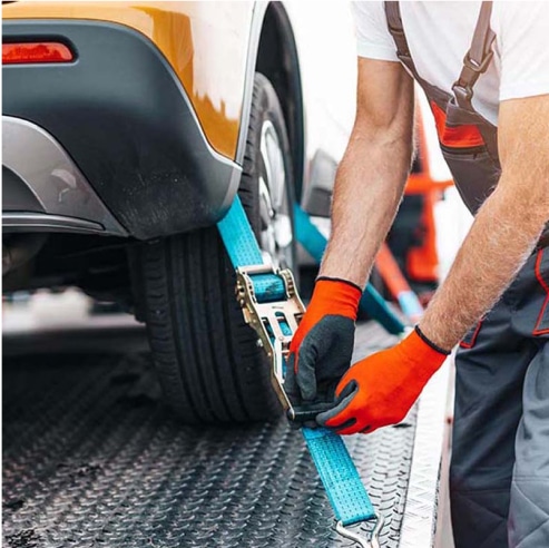 Man securing a car to a flatbed tow truck.