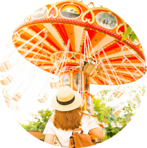 A woman wearing a hat looks at carnival ride with swings.