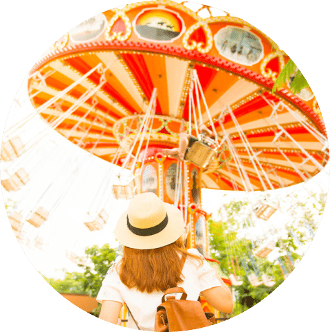 A woman wearing a hat looks at carnival ride with swings.