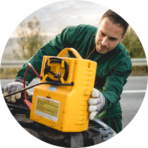 A man holds a yellow battery charger on top of a car.