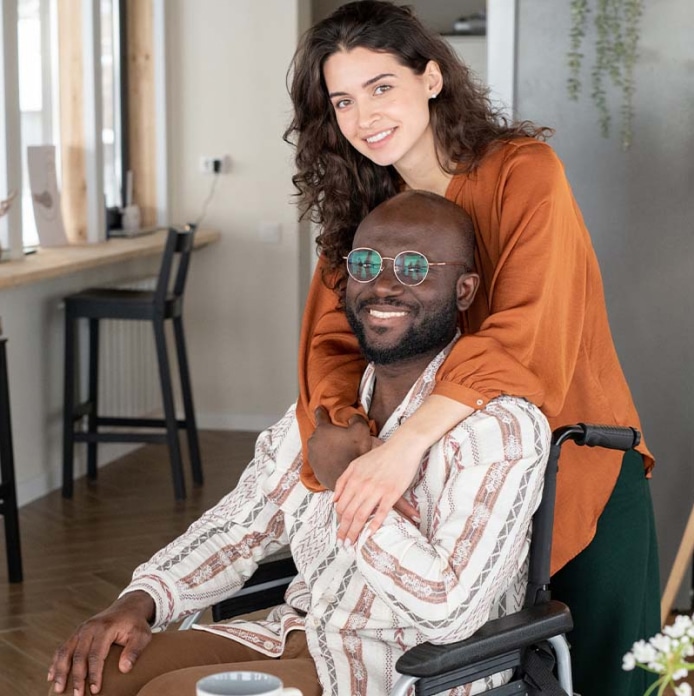 Woman with arms around a smiling man in a wheelchair.