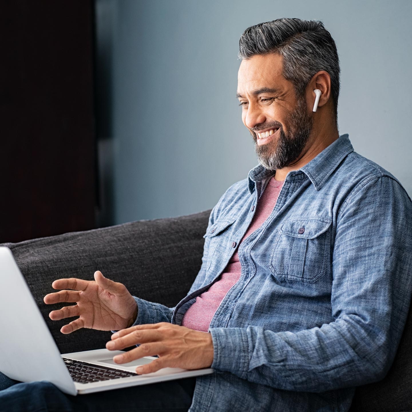 Smiling man working on a laptop and wearing ear pods.