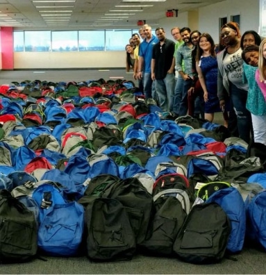 Group of volunteers standing next to backpack donations.