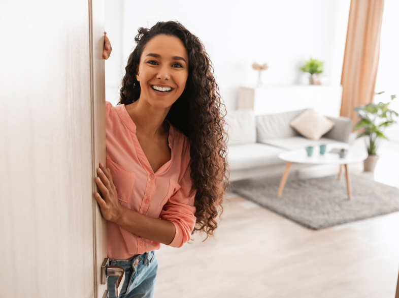 Smiling woman opening a door to a living room.
