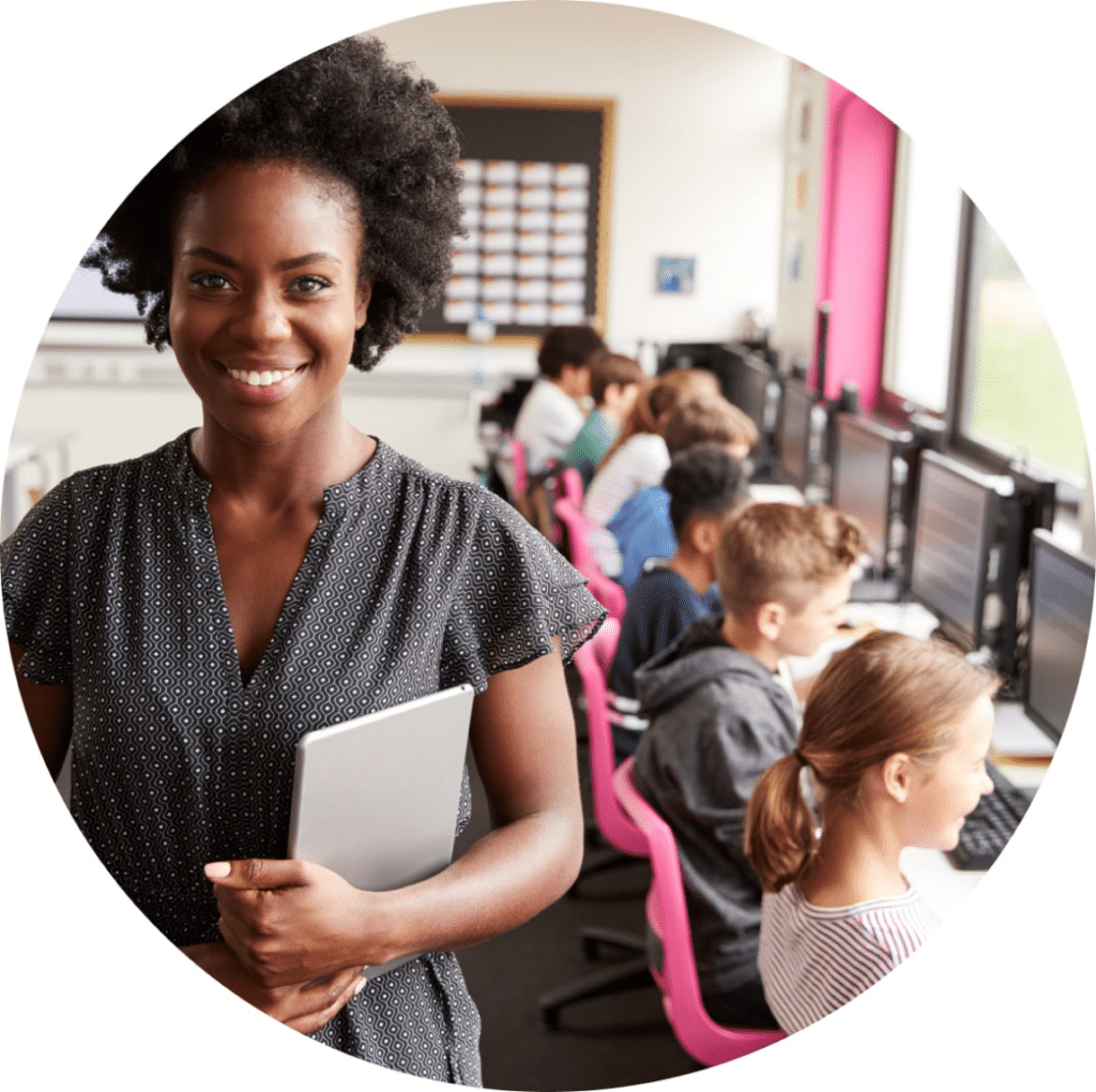 Smiling woman holding a laptop in a classroom with children.