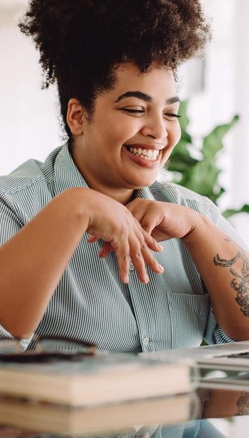 remote-work-opportunity Smiling woman with a tattoo looking at a laptop.